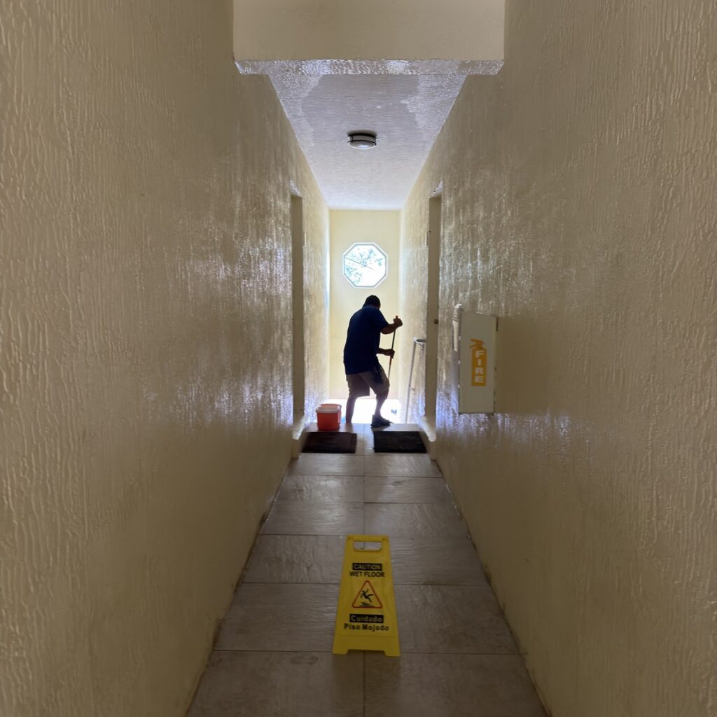 Worker cleaning a common-area corridor with a wet-floor caution sign