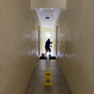 Worker cleaning a common-area corridor with a wet-floor caution sign